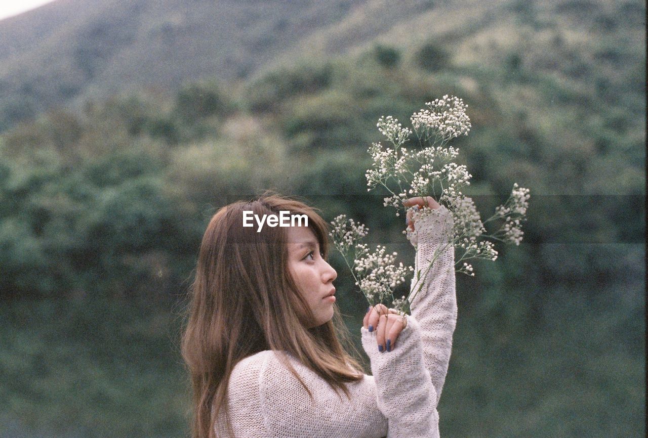 Side view of young woman holding flowers