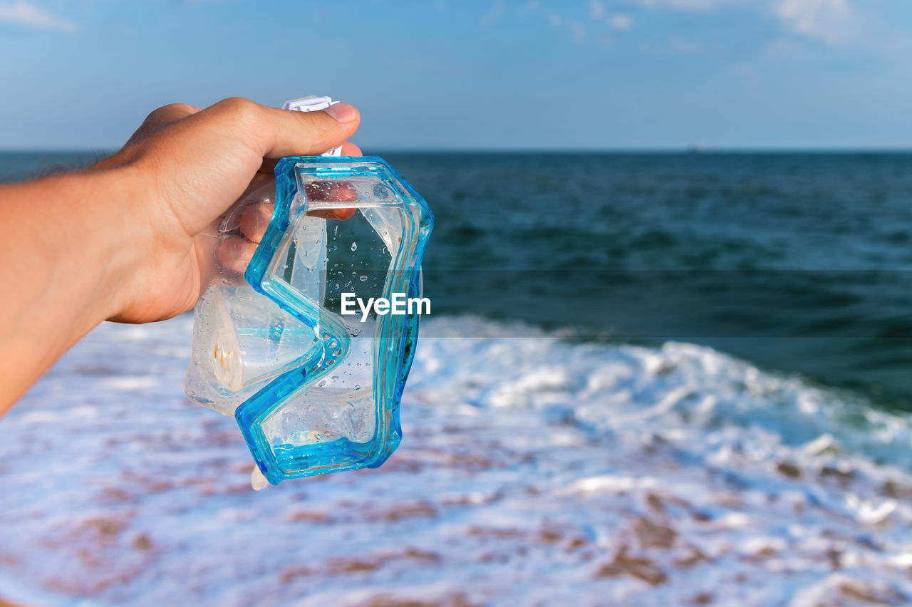 Hand holds snorkeling goggles against the background of the sea or ocean and sky. diving goggles and