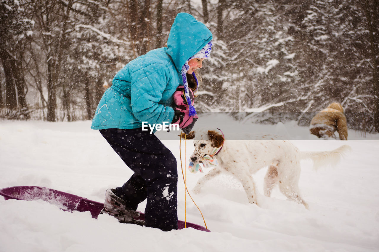 Side view of girl sledding by dog on snow covered field