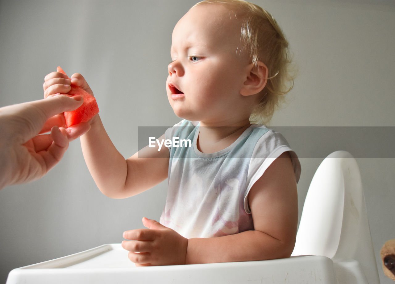 Mom gives a piece of watermelon to her almost 2 years old baby girl.