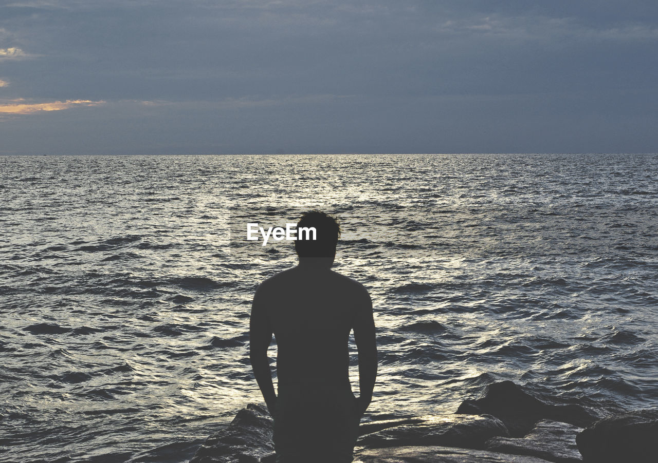 Man standing at beach against sky during sunset