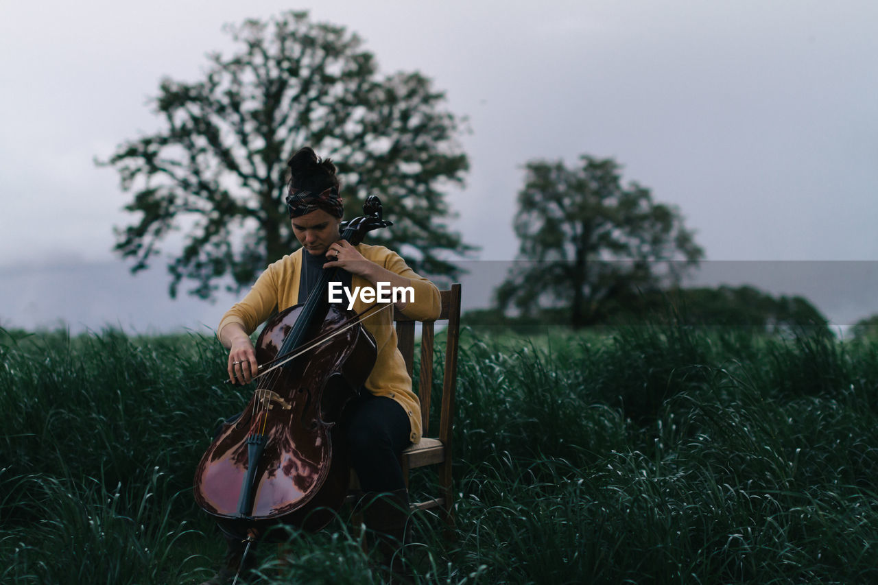 Young woman playing cello on field against sky