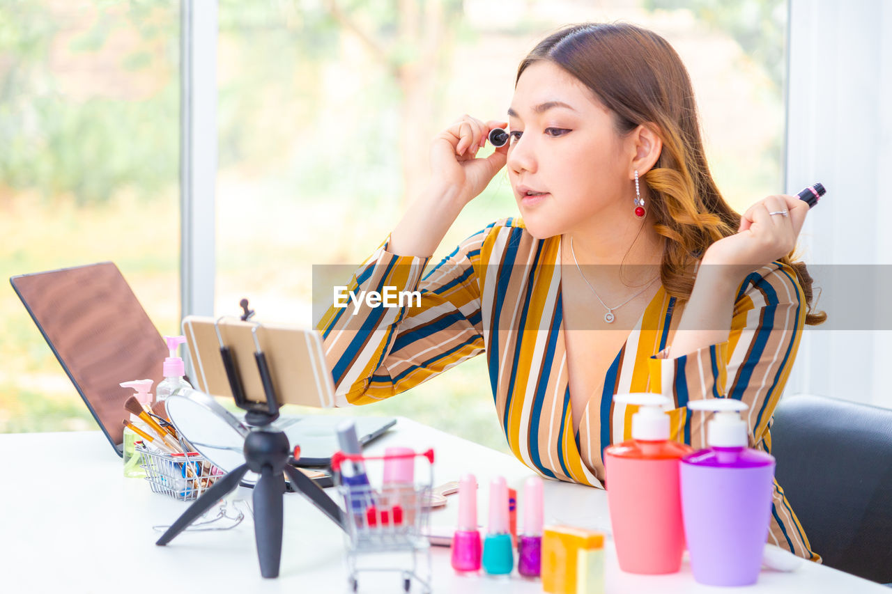 Young woman blogging while applying beauty product on table
