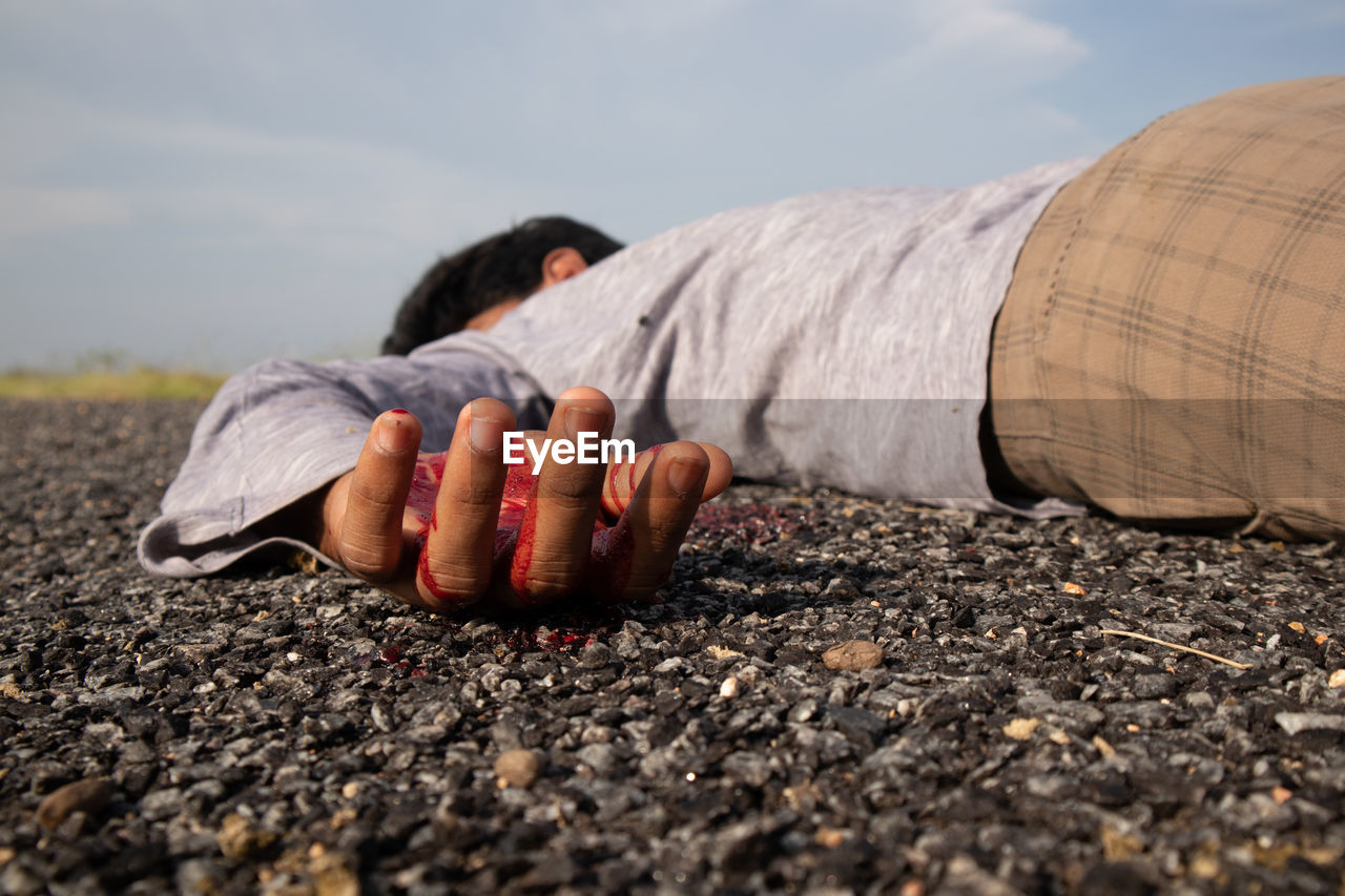 Close-up of man lying down on road against sky