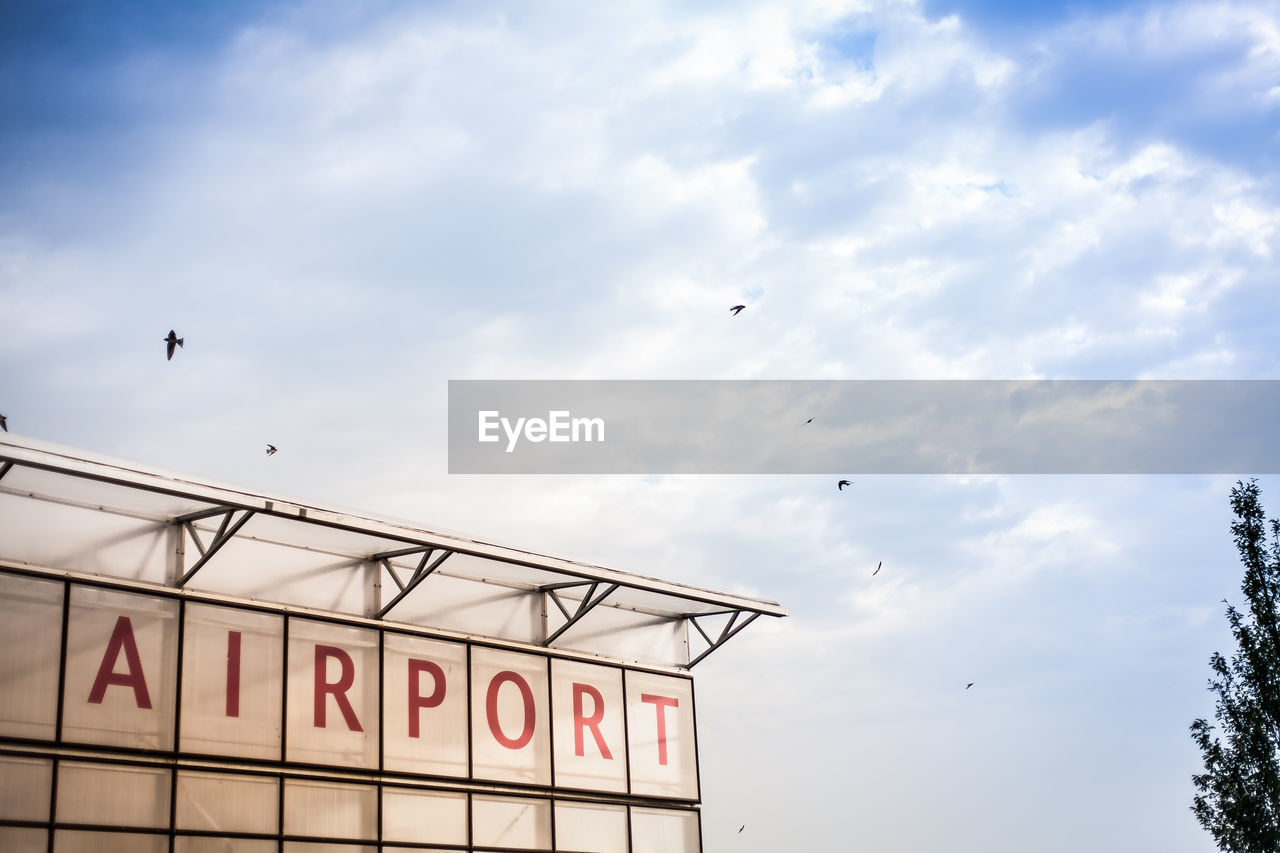 Low angle view of bird flying against cloudy sky at airport