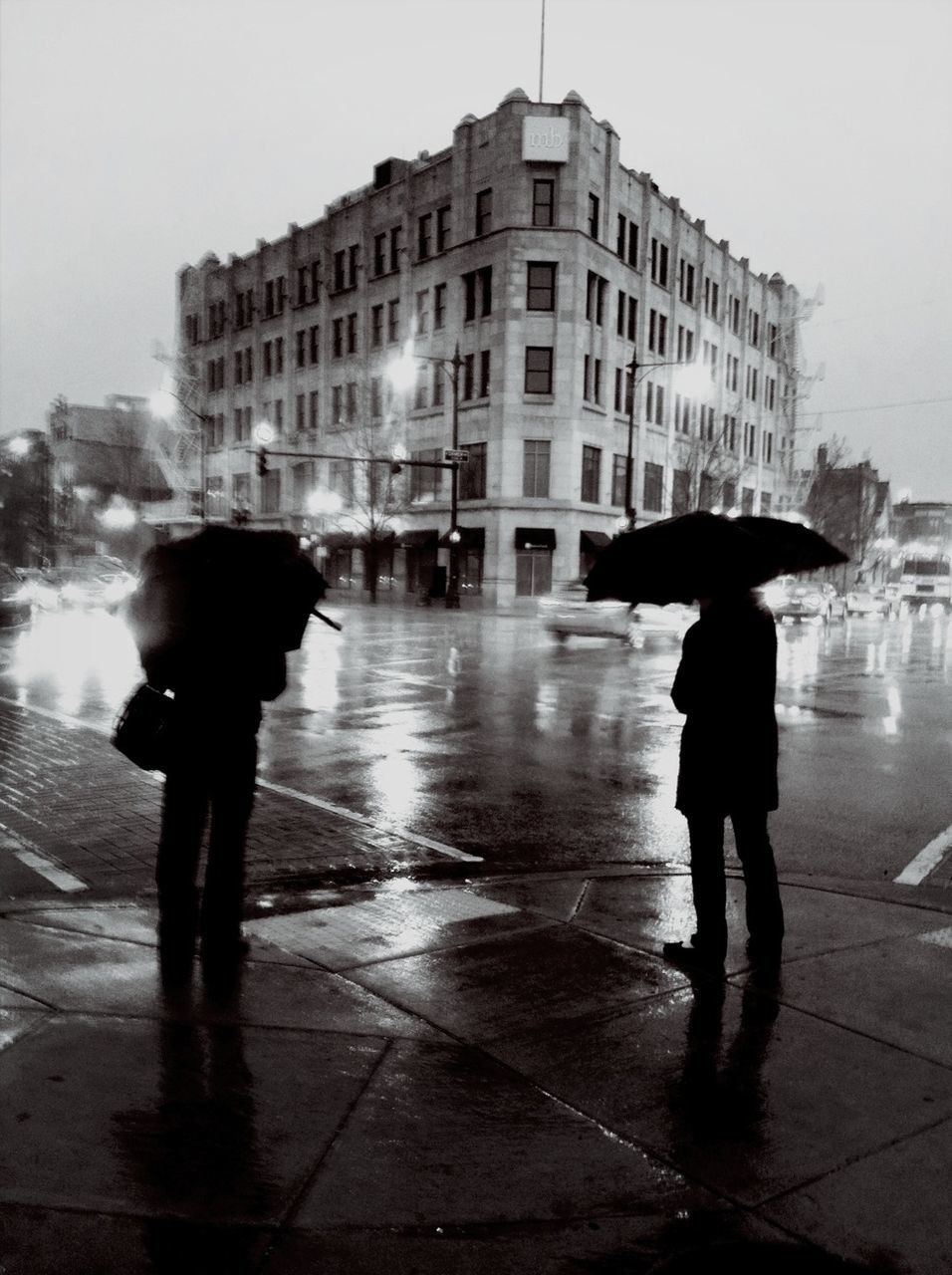 Silhouette people with umbrellas standing on sidewalk during rainy season
