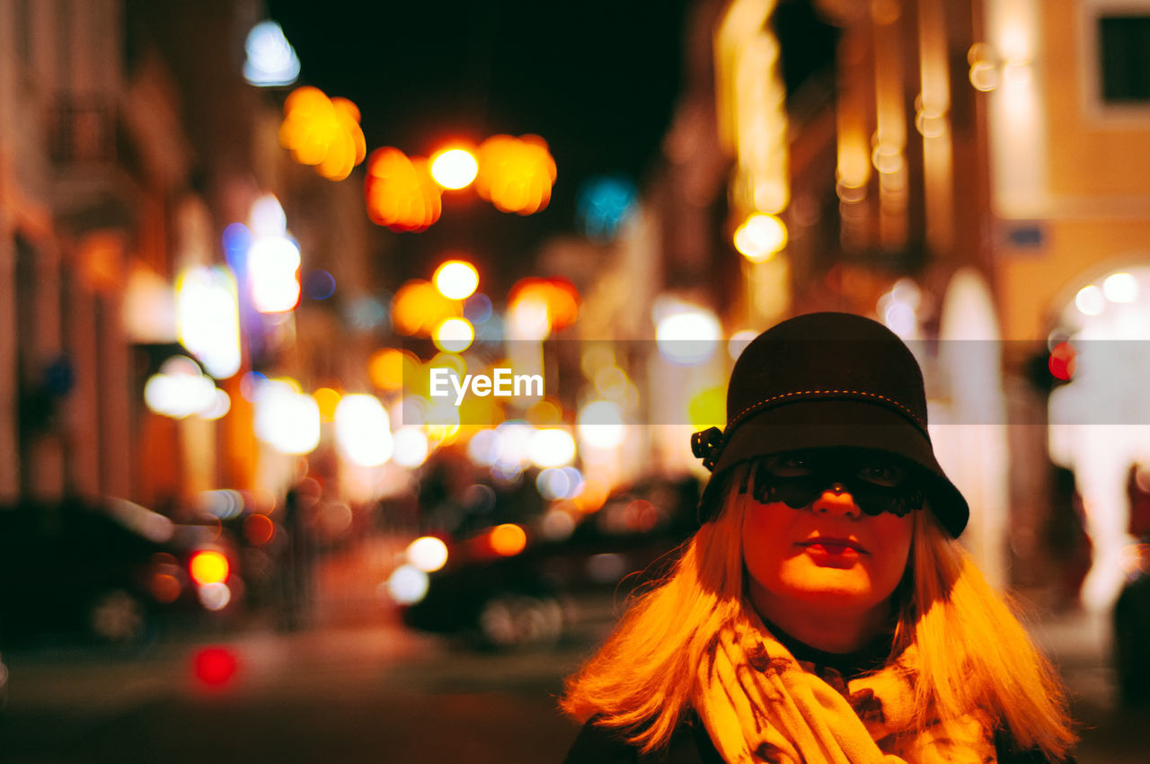 Portrait of woman standing on illuminated street at night