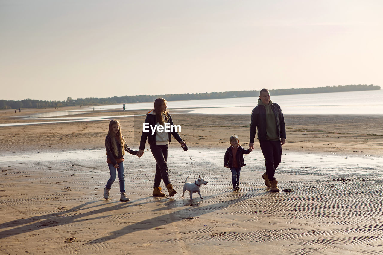 Family in a leather jacket walks along the beach with their dog in autumn