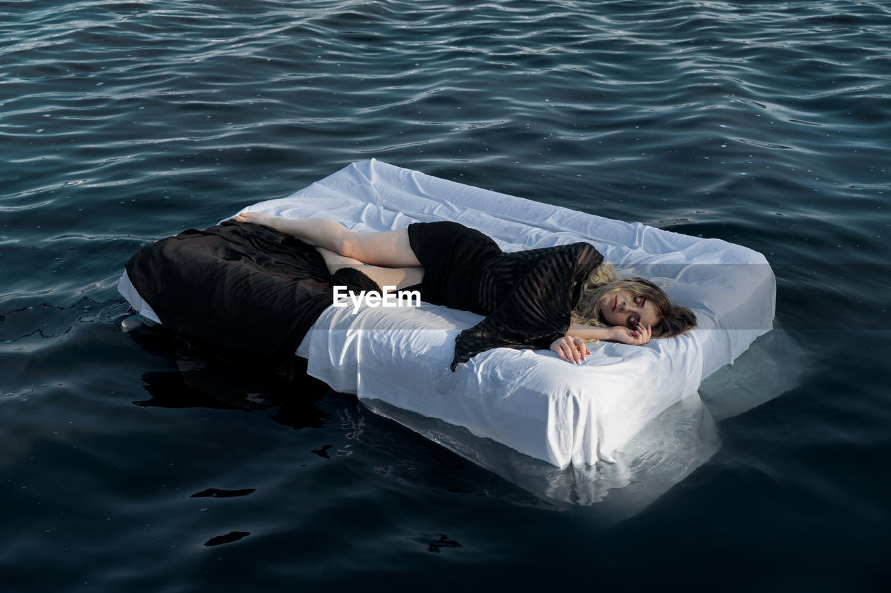 High angle view of woman sleeping on mattress in sea