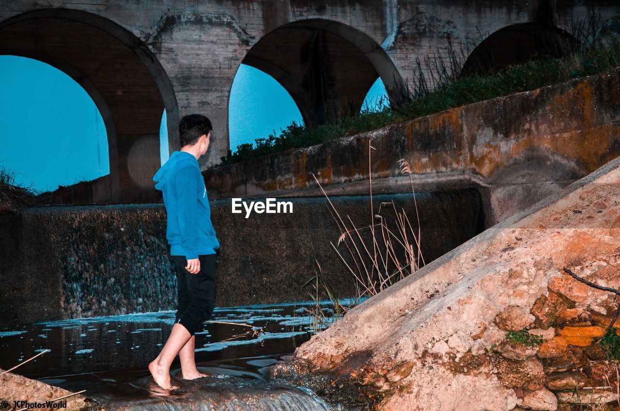 Man walking in dam against arch bridge