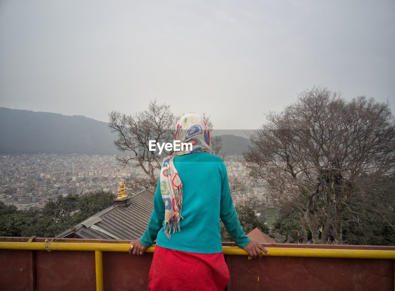 Rear view of woman leaning on railing against clear sky