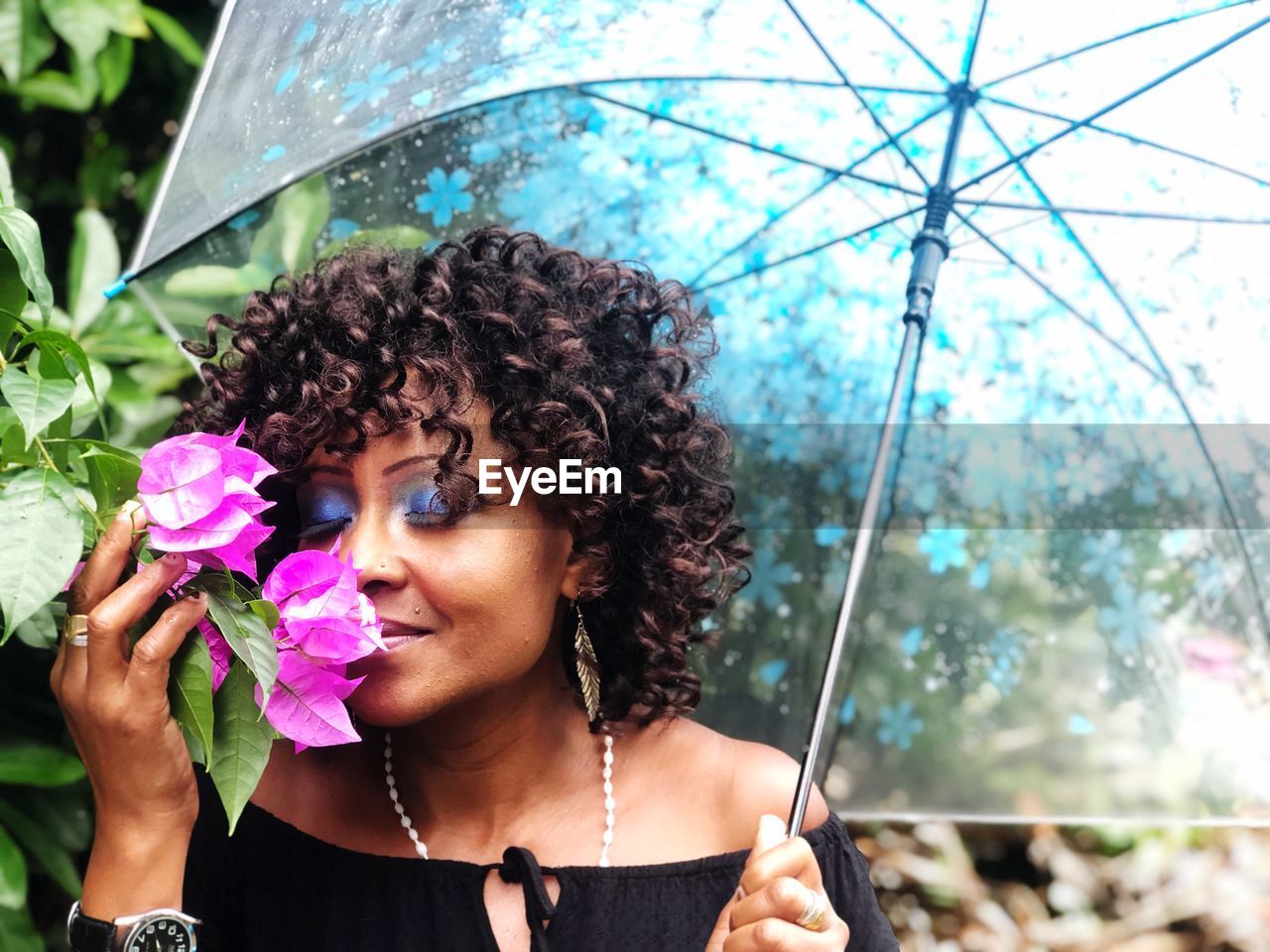 Mature woman with curly hair holding umbrella while smelling flowers