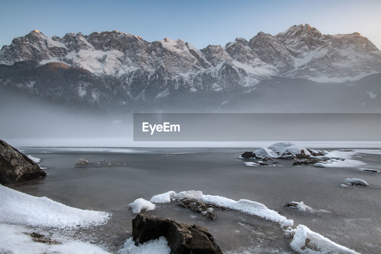 Scenic view of frozen lake by mountains against sky