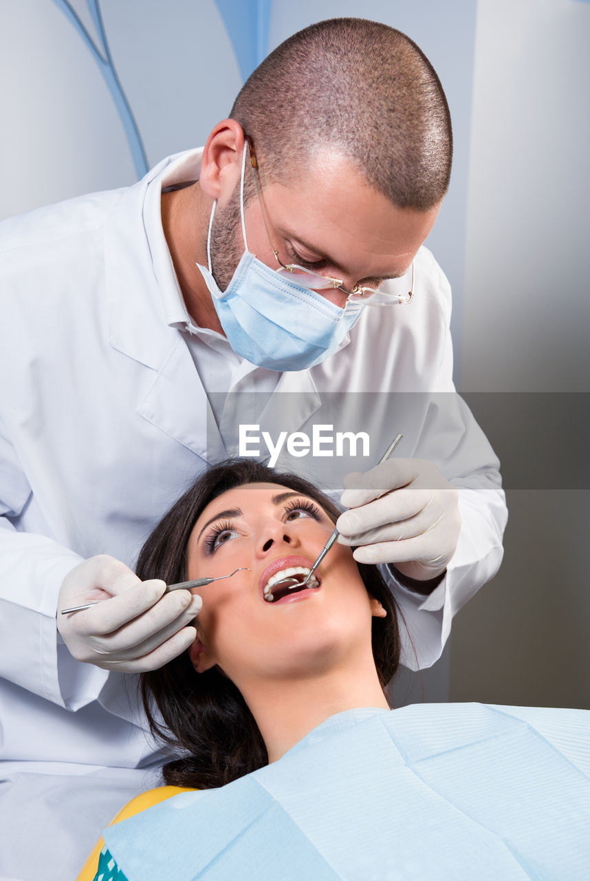 Male dentist operating female patient in clinic