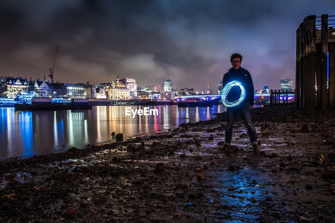 Full length of man spinning illuminated wire wool by river thames at night