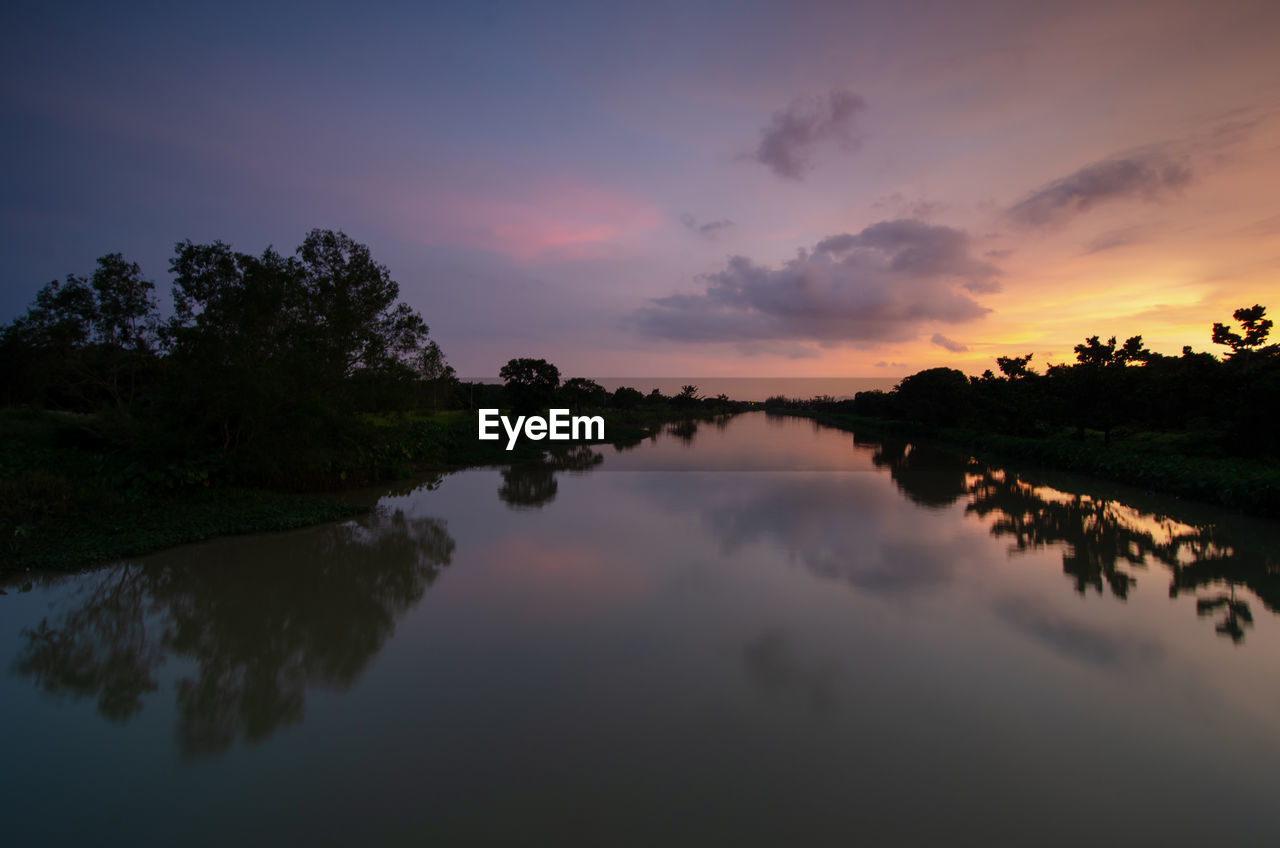 reflection, water, sky, morning, dawn, environment, beauty in nature, scenics - nature, nature, tranquility, tree, landscape, lake, cloud, sunrise, plant, tranquil scene, twilight, sun, no people, land, outdoors, travel destinations, reflection lake, travel, multi colored, idyllic, silhouette, forest, sunlight, non-urban scene, fog, rural scene, orange color, standing water, blue