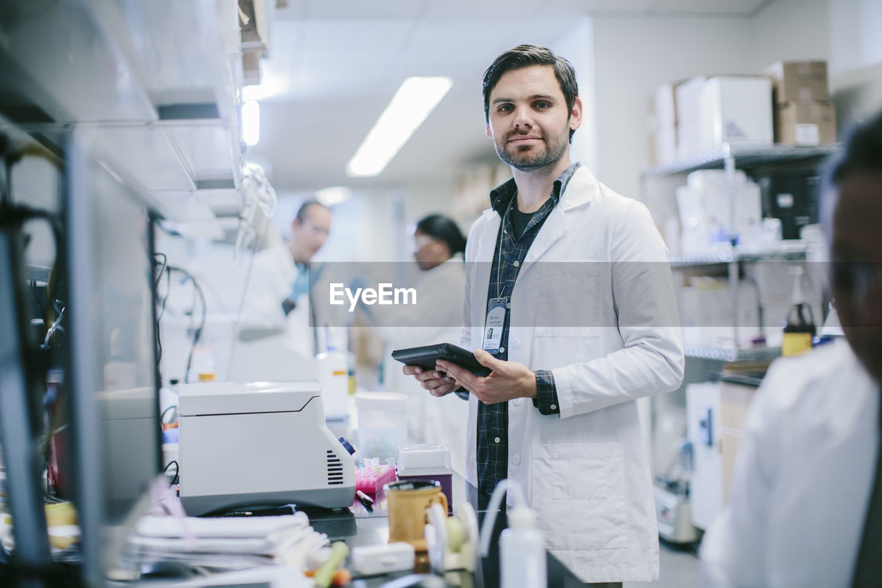 Portrait of male doctor with tablet computer and coworkers working in medical room