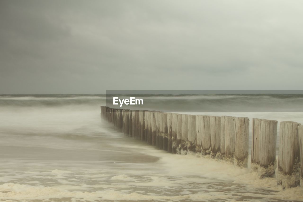 WOODEN POST IN SEA AGAINST SKY