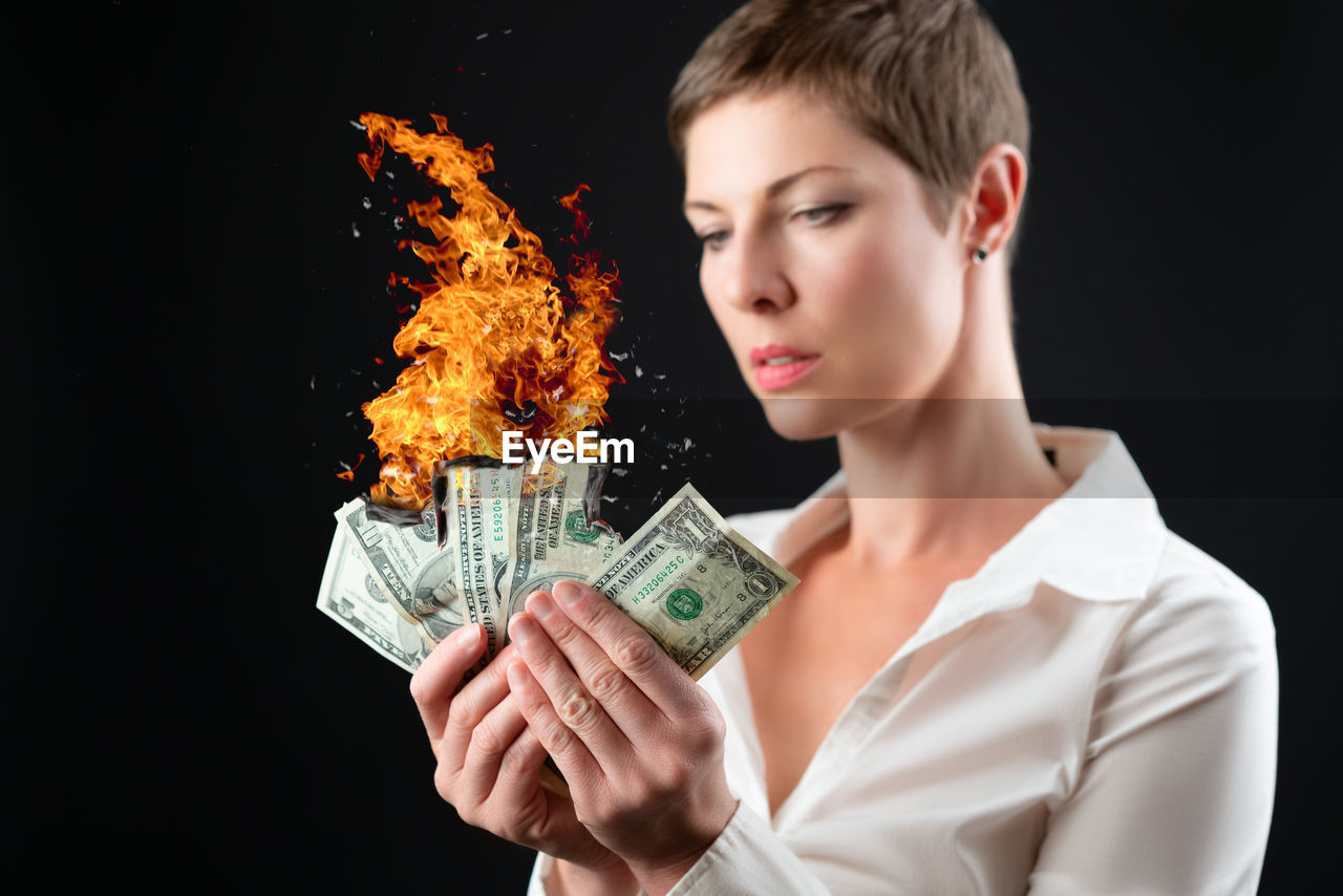 portrait of young woman holding paper currencies against black background