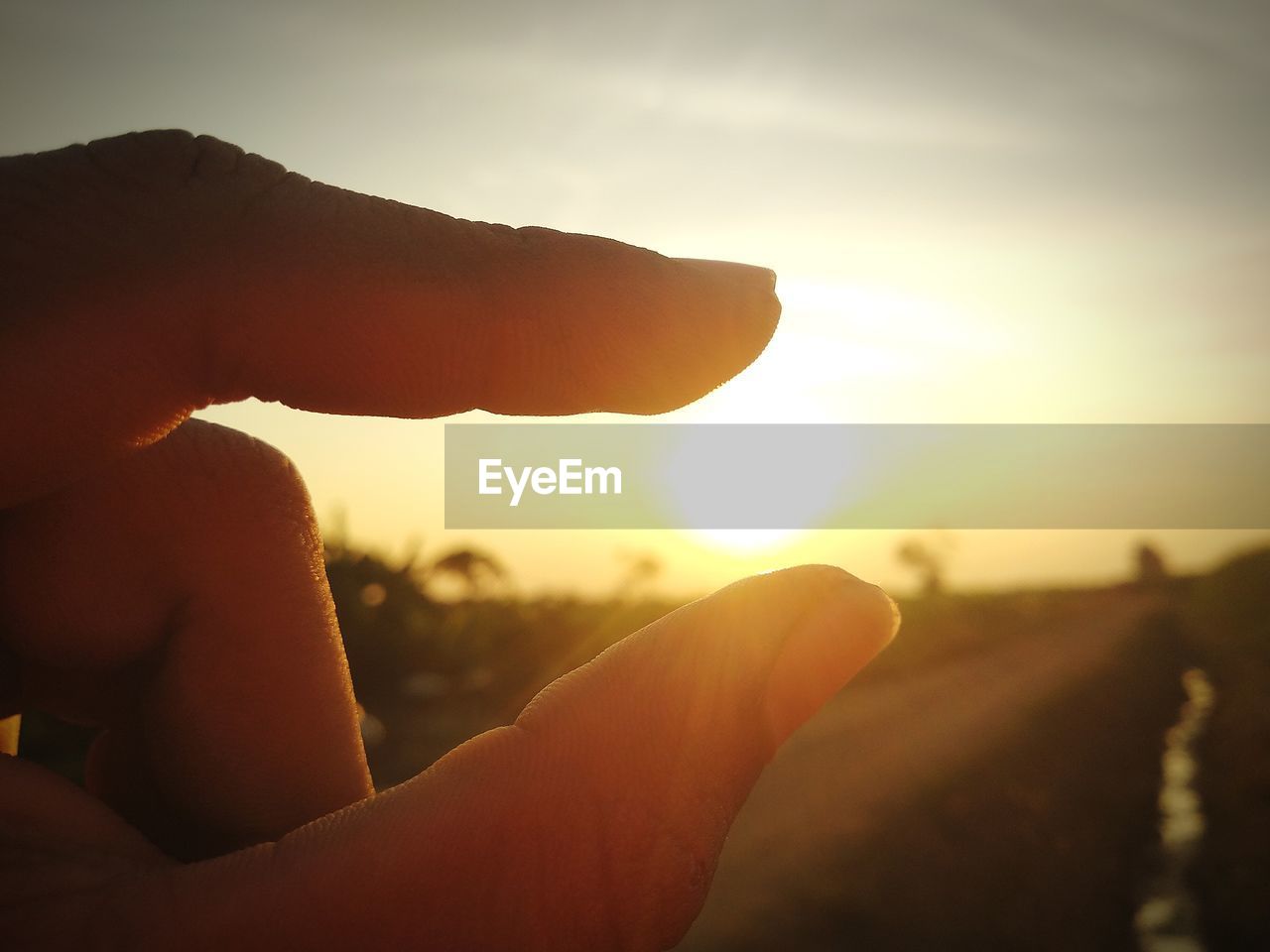 CLOSE-UP OF HAND HOLDING SUN DURING SUNSET AGAINST SKY