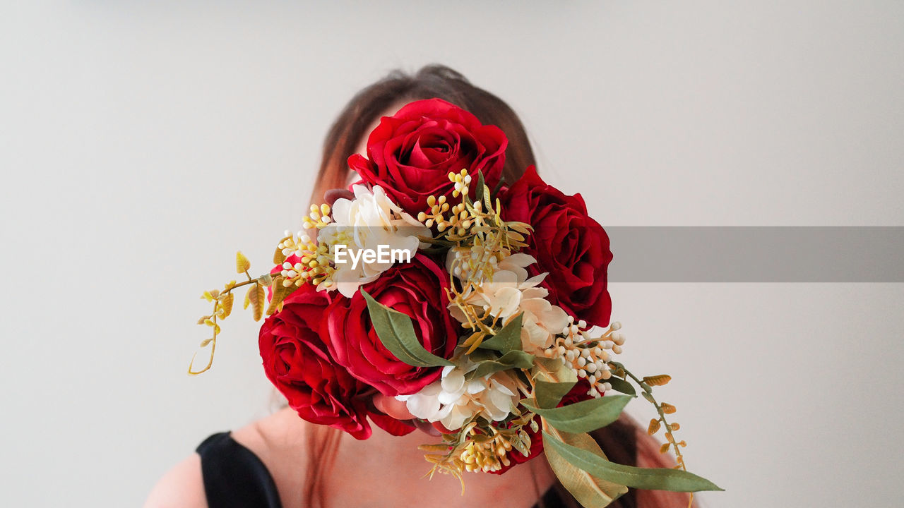 LOW SECTION OF PERSON HOLDING ROSE BOUQUET AGAINST RED WALL