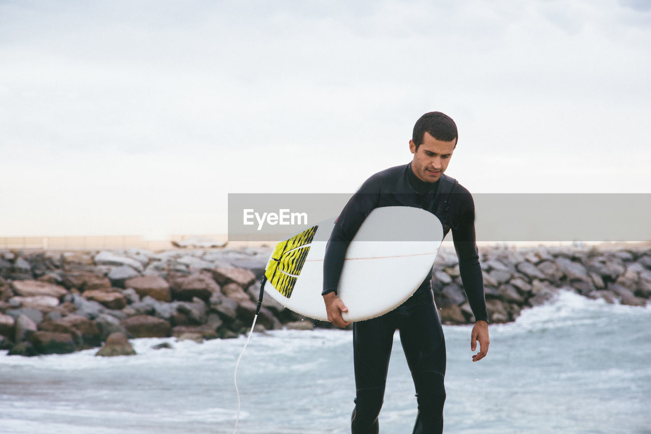 Man carrying surfboard while walking on shore at beach