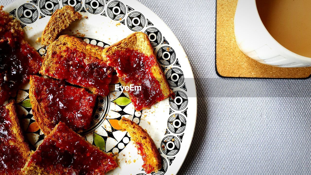 Cherry jam on toasted bread with tea on table