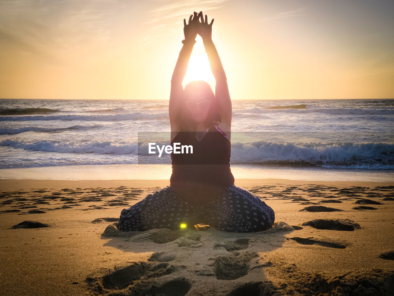 View of woman doing yoga at beach against sky during sunset