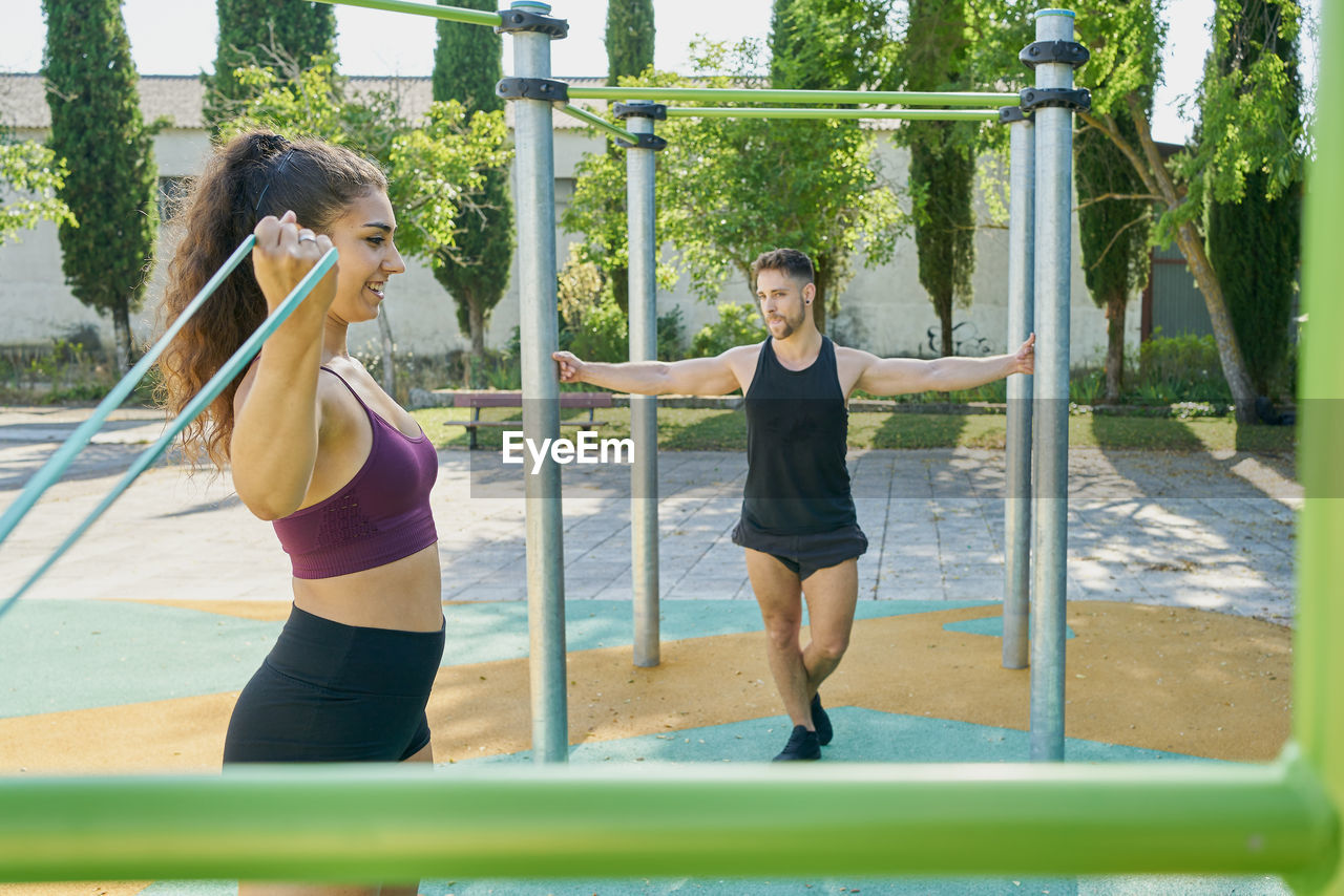 Young woman and man practicing calisthenics in a park on sunny day