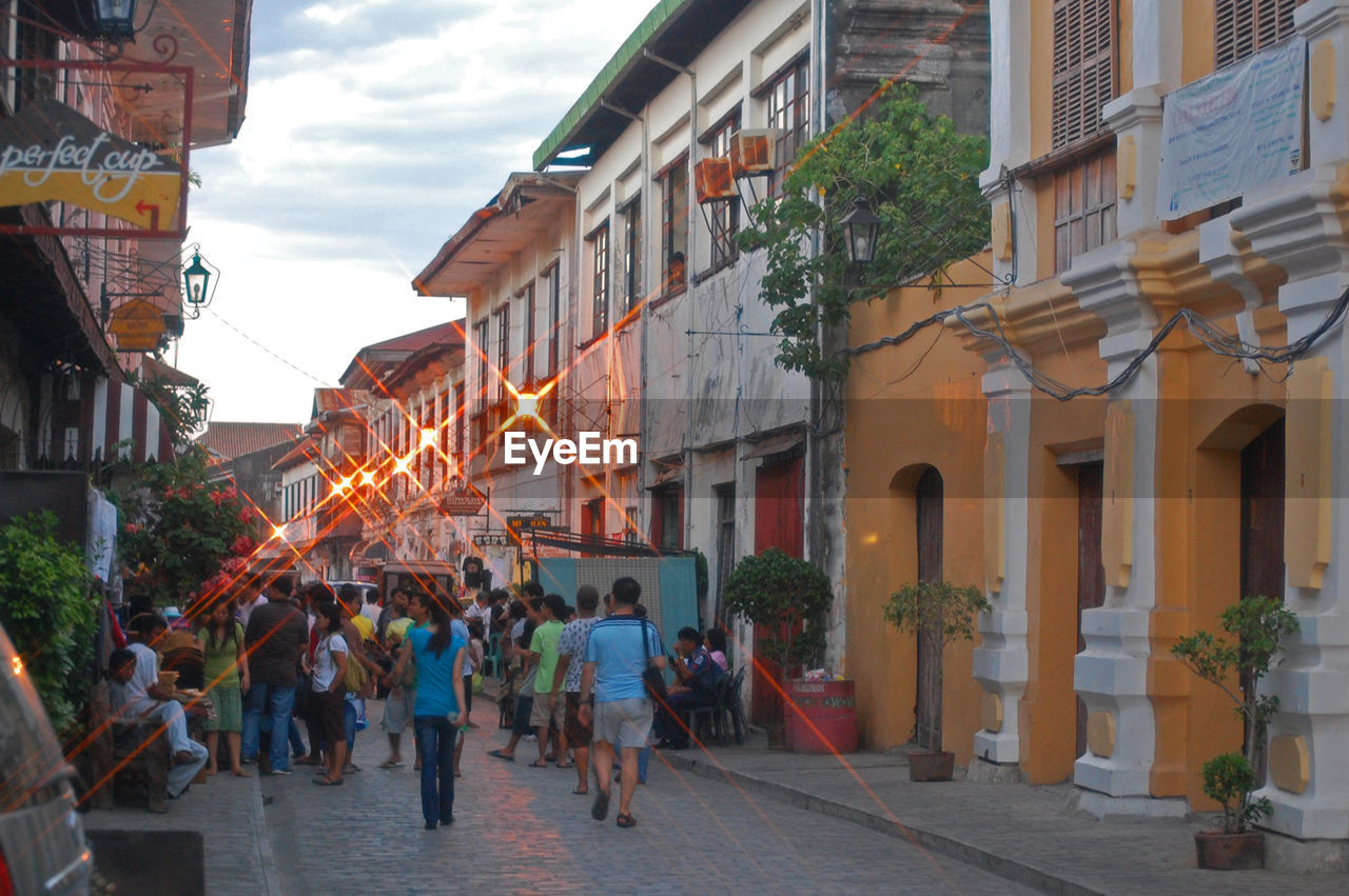 GROUP OF PEOPLE WALKING ON STREET AMIDST BUILDINGS