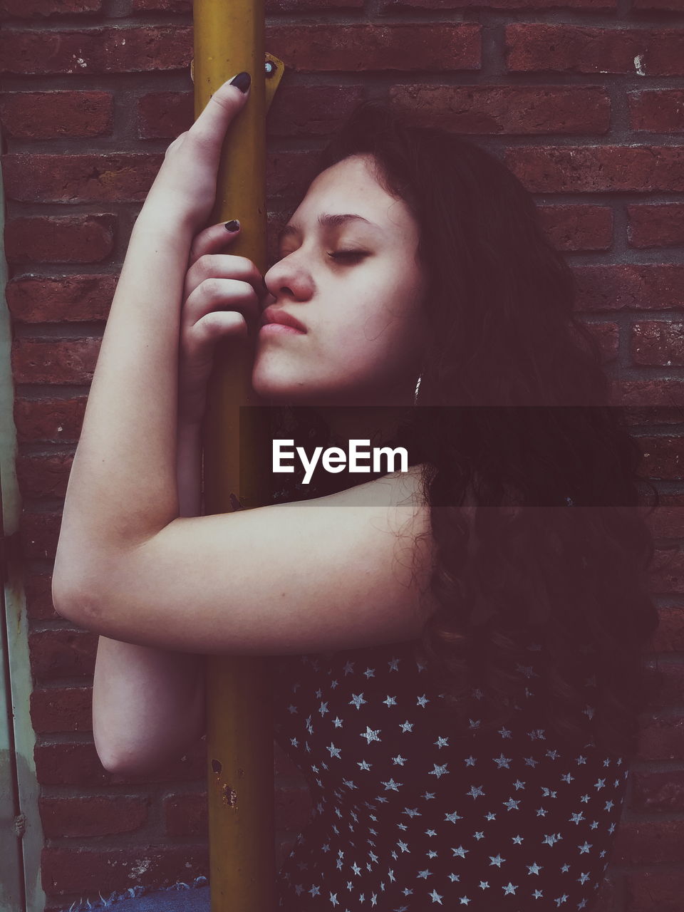 Young woman embracing pole against brick wall