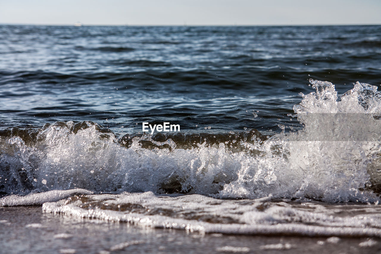 Waves splashing on sea against clear sky