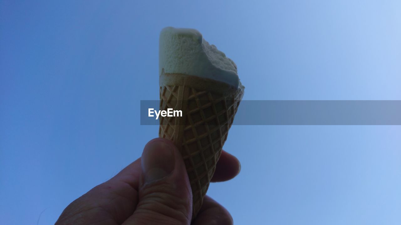 Hand holding ice cream against blue sky