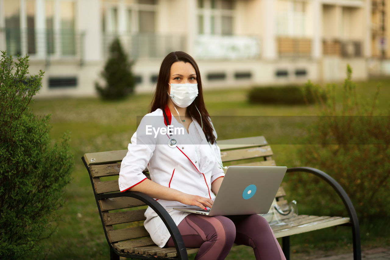 young woman using phone while sitting on chair at park