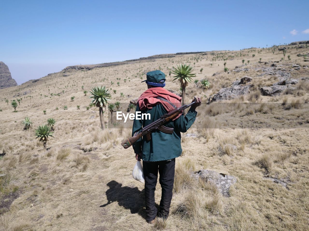 Rear view of man with rifle standing on field