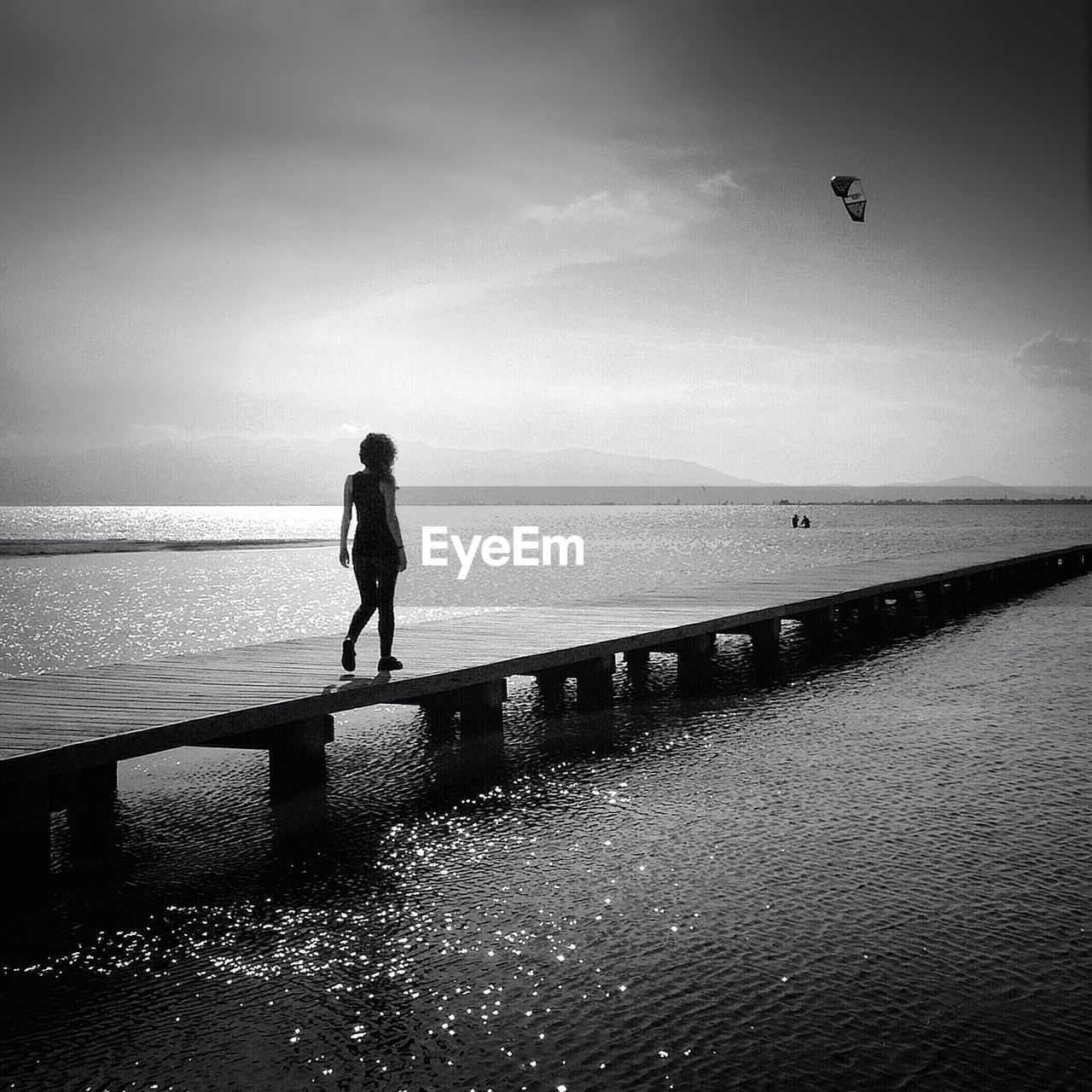 Full length rear view of woman walking on pier amidst lake against sky