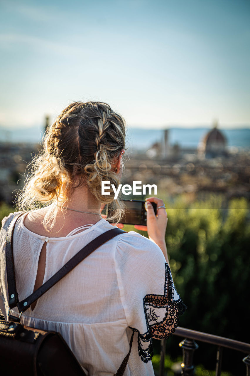 Rear view of woman looking at cityscape against sky