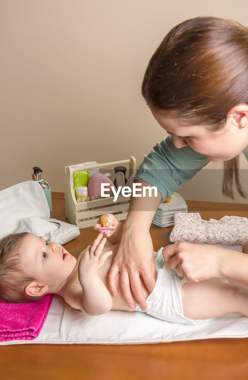 Woman changing diaper of baby girl at home