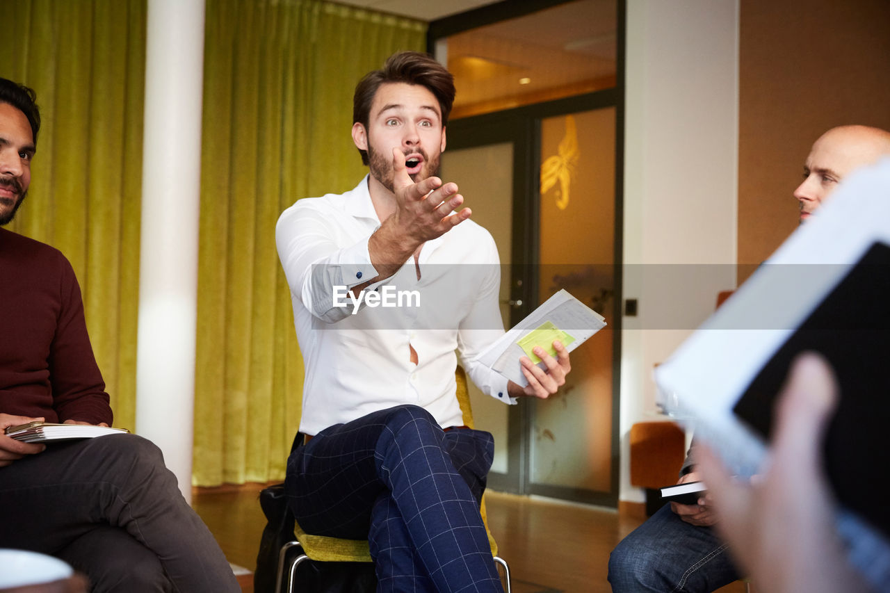Shocked businessman discussing with colleagues while sitting in office seminar