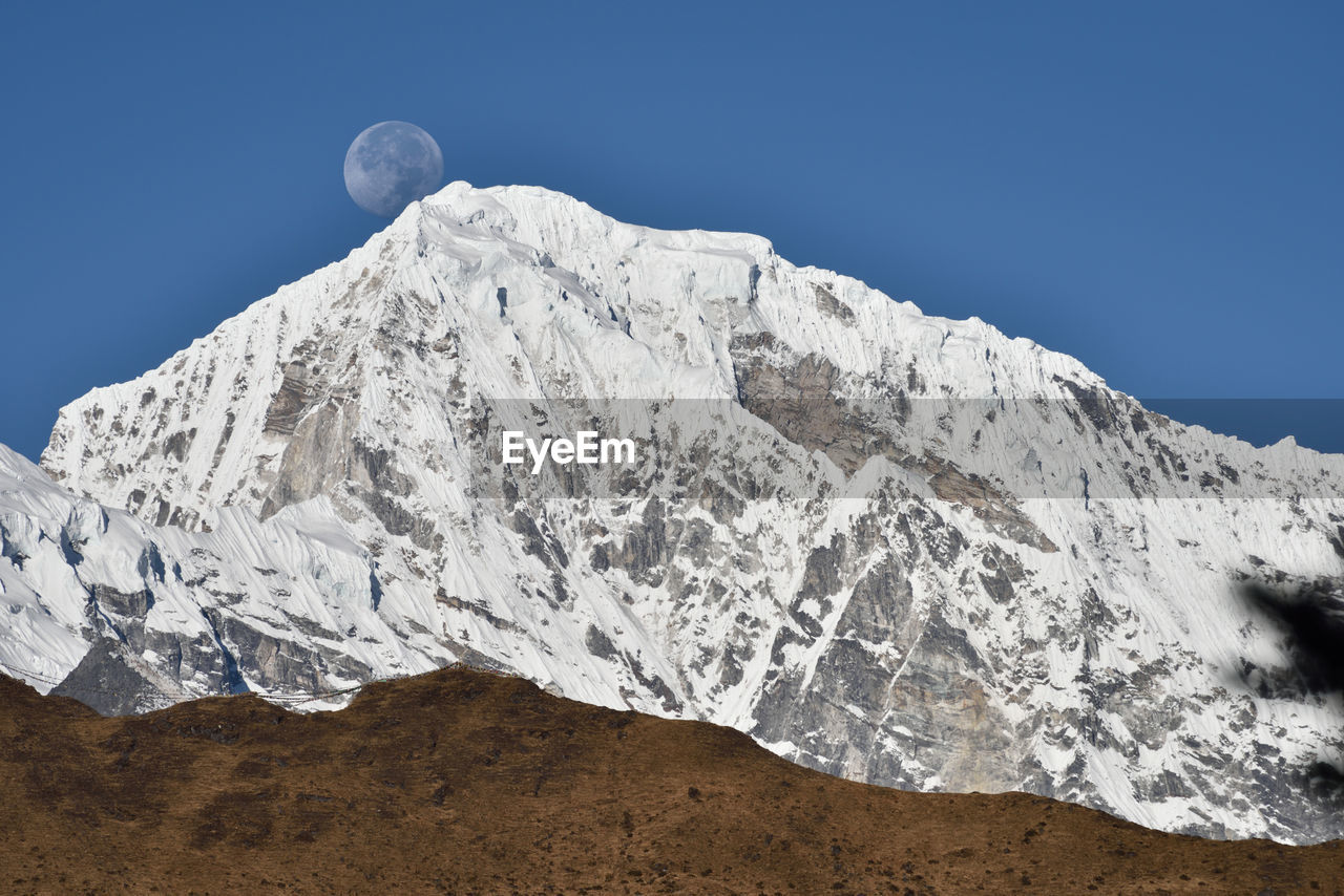 Scenic view of the moon behind snowy mountains 