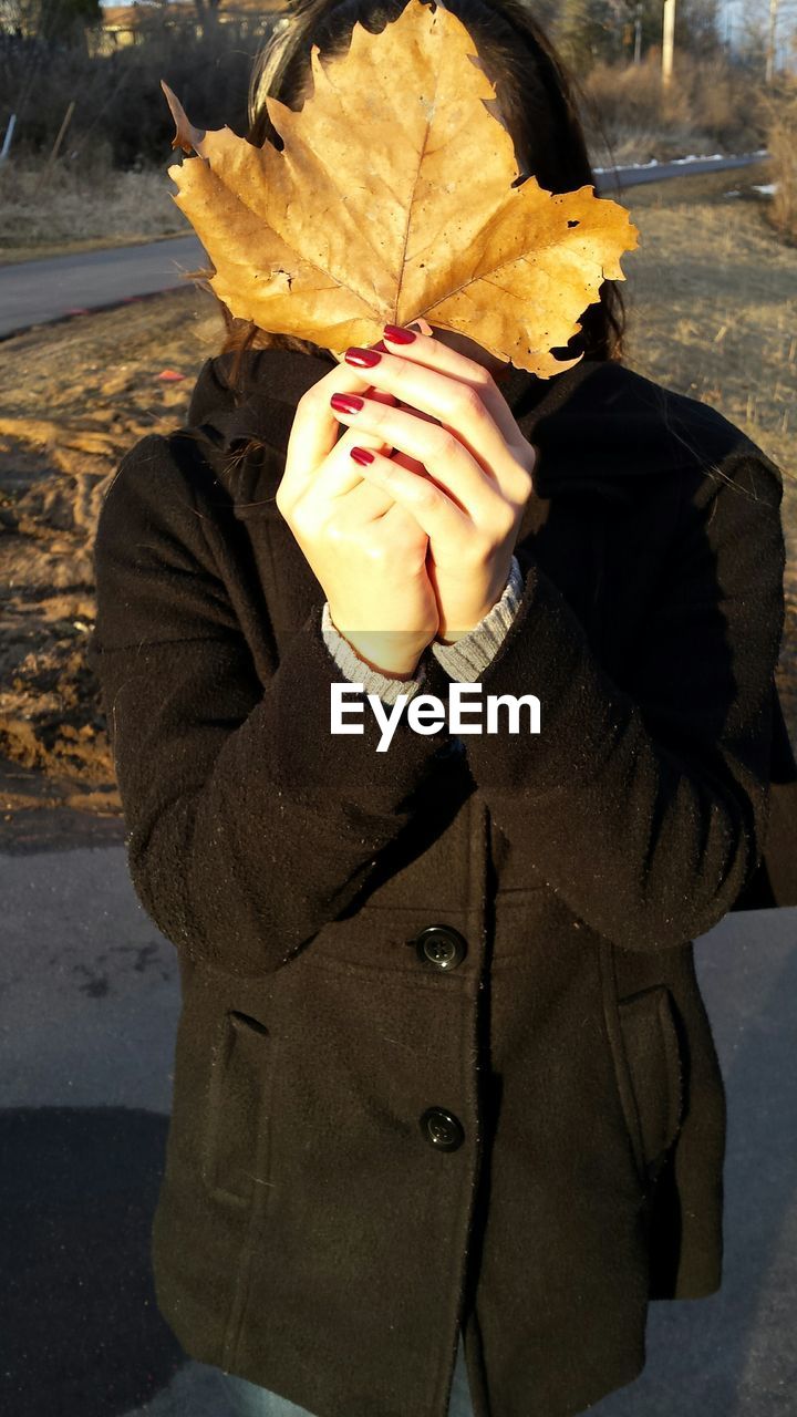 Woman hiding face with dry leaf on field