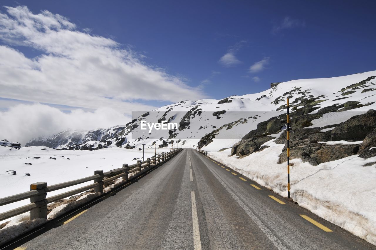 Empty road leading towards snowcapped mountains during winter