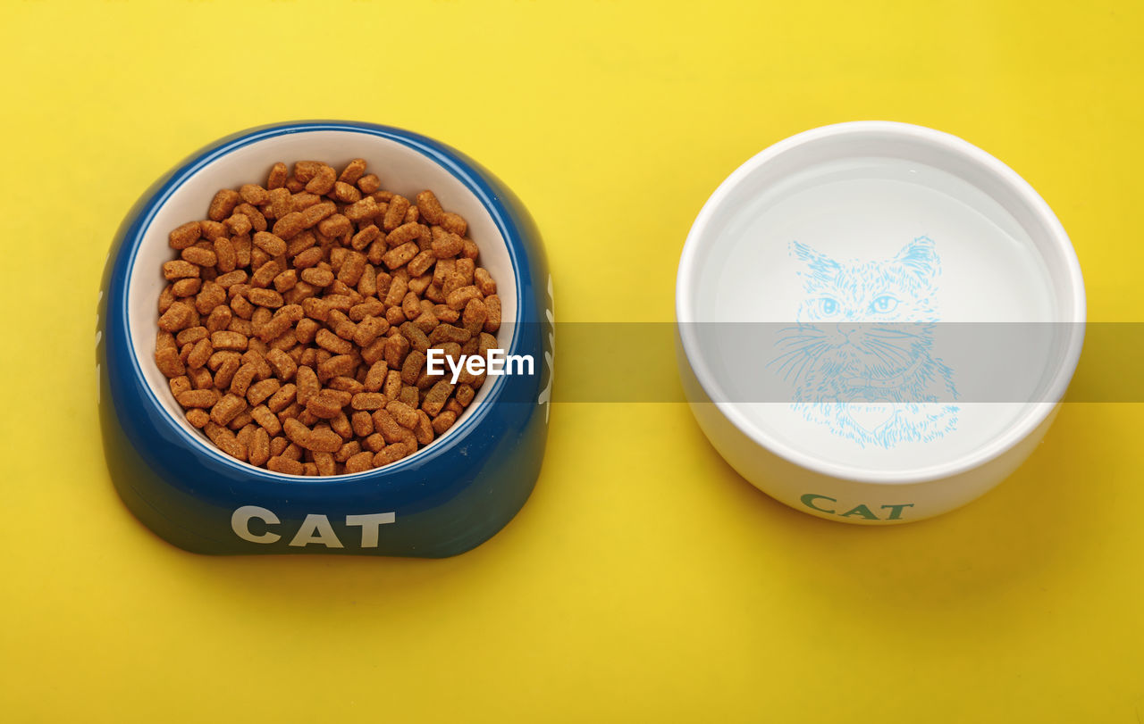 High angle view of cat food and water in bowl over yellow background