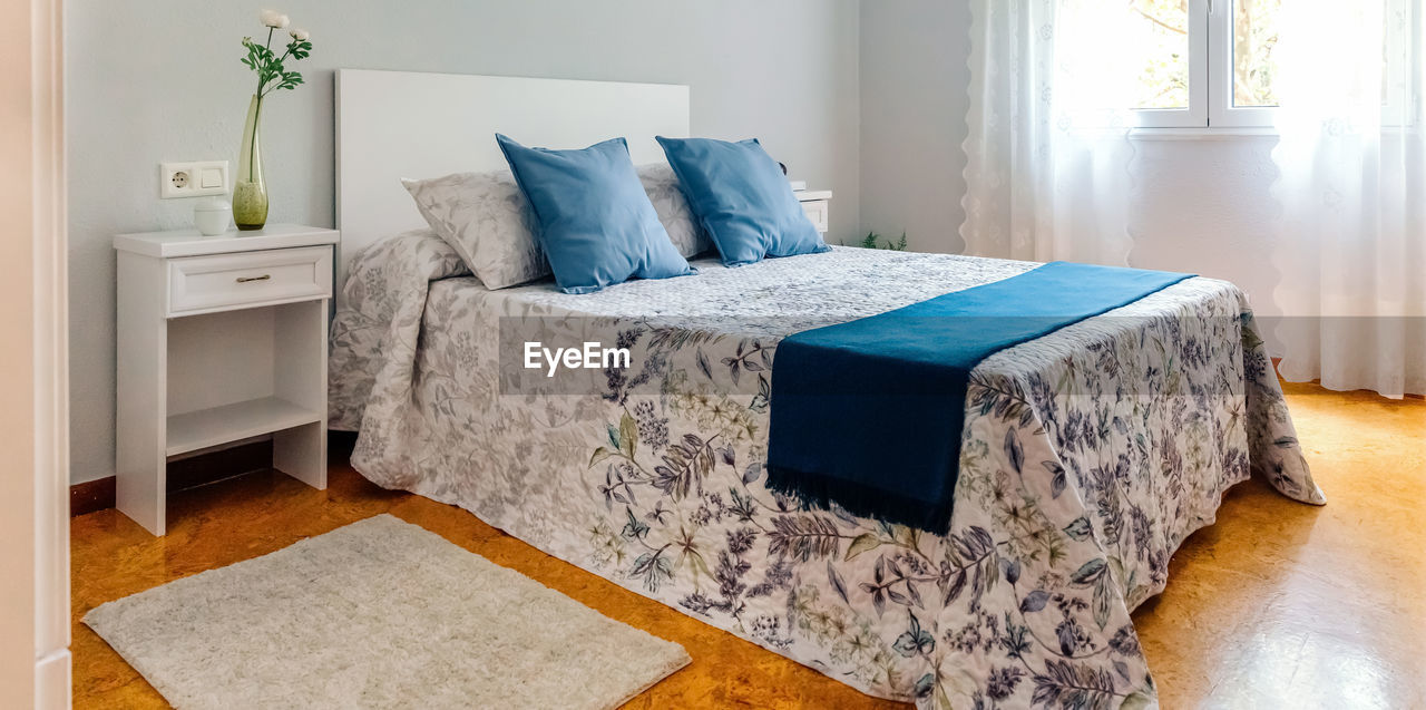 Interior of cozy double bedroom decorated with quilt and curtains