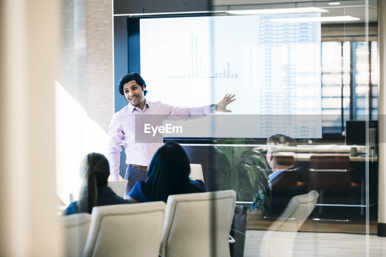 Businessman giving presentation in meeting seen through window