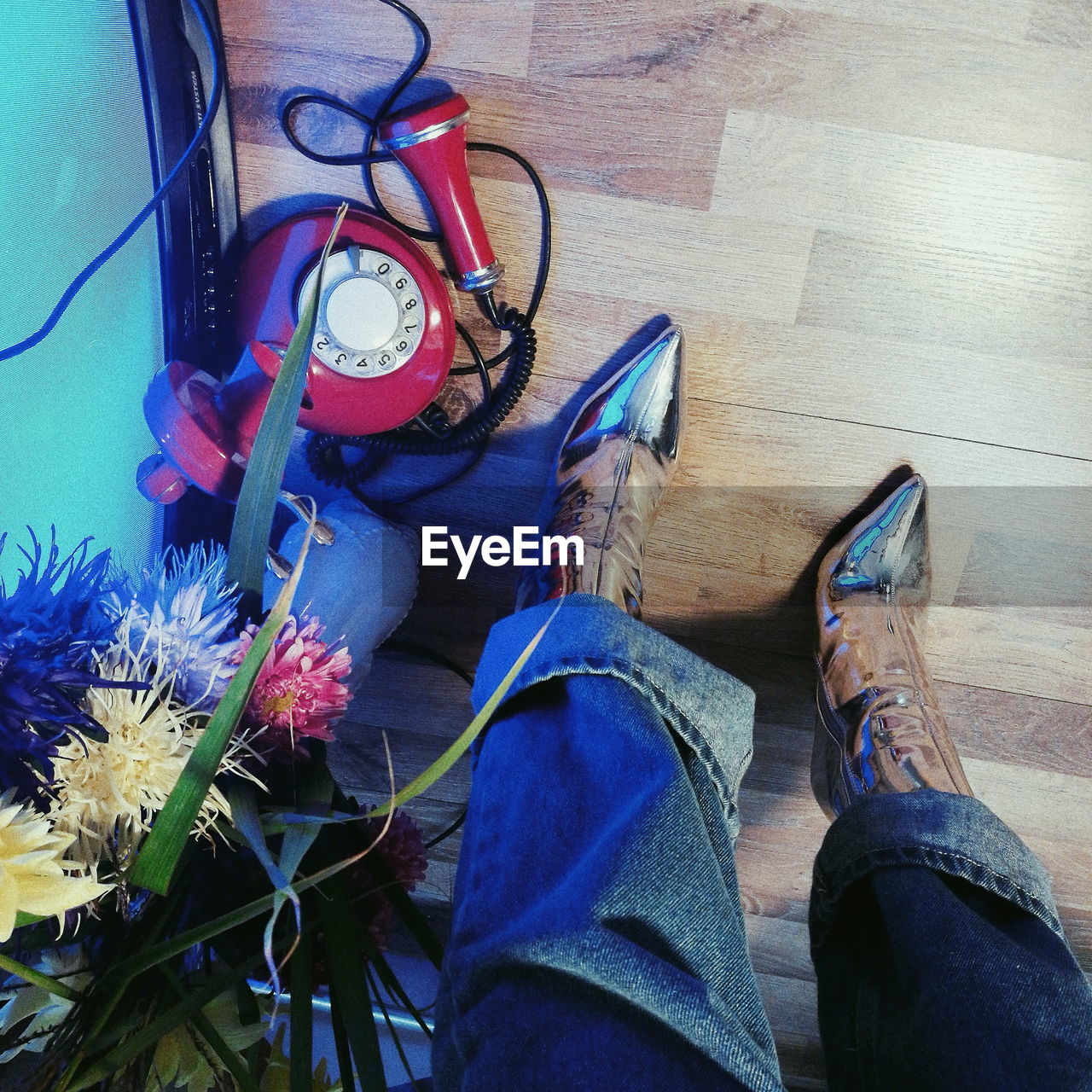 Low section of woman wearing shoes by telephone and flowers on hardwood floor