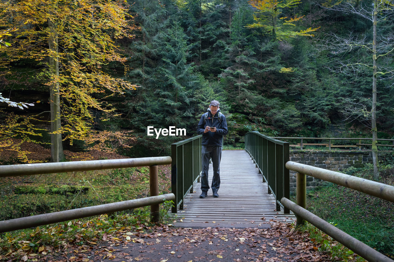 Adult man standing on a footbridge and looking into a digital map on his mobile phone