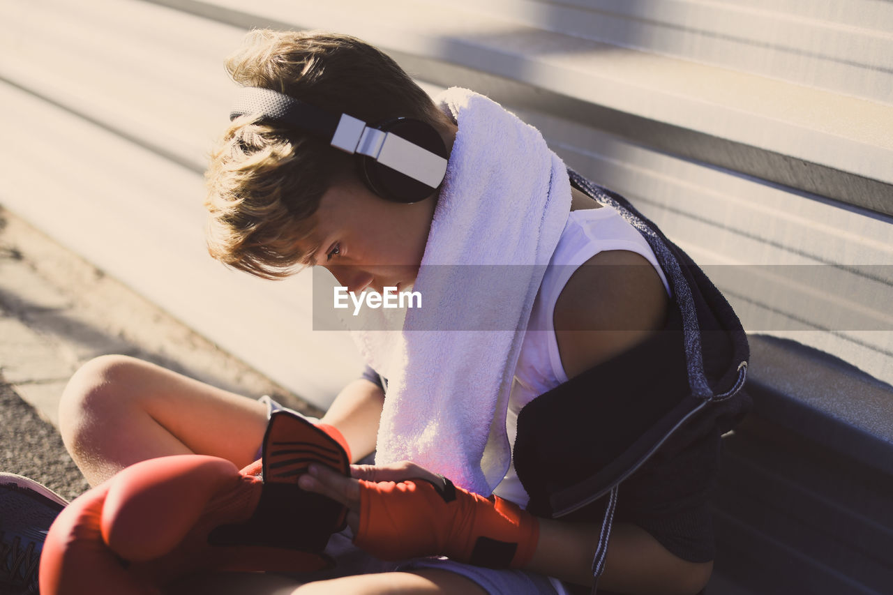 Boy wearing boxing glove while sitting outdoors