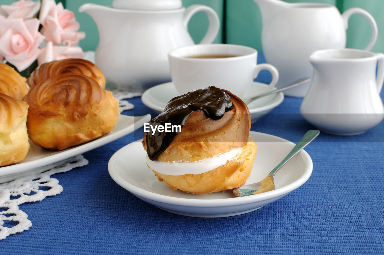 Éclair with chocolate, close-up on a plate with a cup of coffee