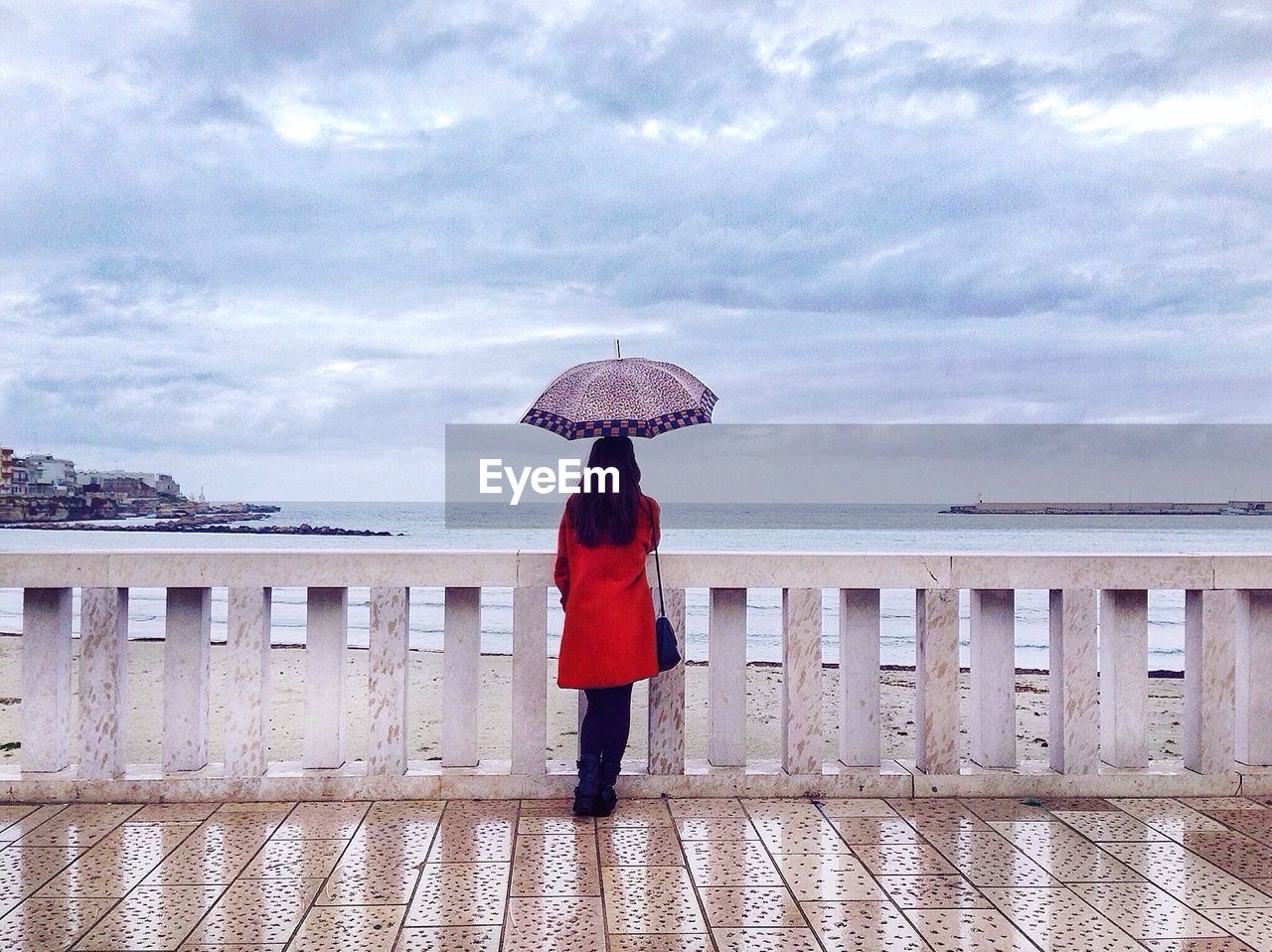 REAR VIEW OF WOMAN STANDING BY RAILING AGAINST CLOUDY SKY